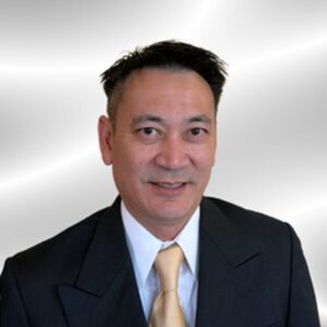 Professional headshot of a man in a dark suit with a beige tie, smiling against a light gray background.